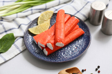 Plate with tasty crab sticks, slices of lemon and green onion on grey background © Pixel-Shot