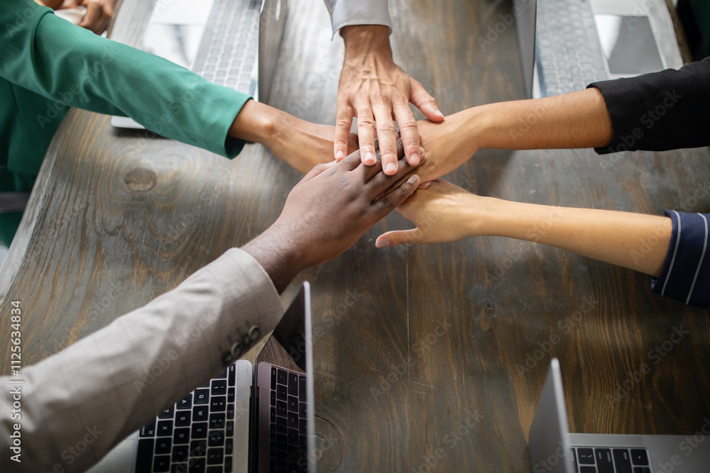 Poster diverse team members gather around a table in a corporate office, joining hands in a show of coopera