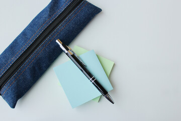 Jeans fabric pencil case, ballpoint pen and pastel color sticky notes on white background with copy space available. Office supplies, stationery, university, back to school concept.