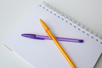 Blank paper page notepad and two color pens on white background. Office supplies. Creative stationery, back to school concept. Purple and orange color ballpoint pen.