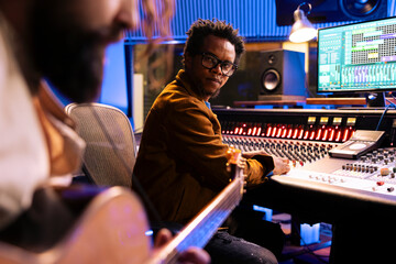 Young musician playing electro acoustic guitar and recording tunes in studio, using musical instrument to compose a new tracks. Singer and sound designer working on a new pop rock album.