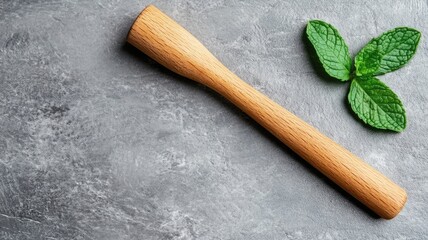 Wooden muddler and mint leaves on gray surface
