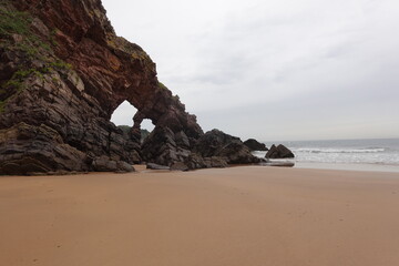 Eroded rock formation creating natural arch on sandy beach - Powered by Adobe