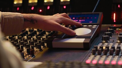 Audio technician uses mixing console and faders in control room, remote control for adjusting sound...