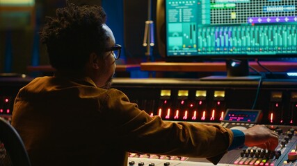 African american producer working at mixing panel in recording studio. Using control desk and...