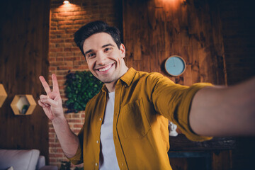 Young man in casual shirt making peace sign and smiling indoors