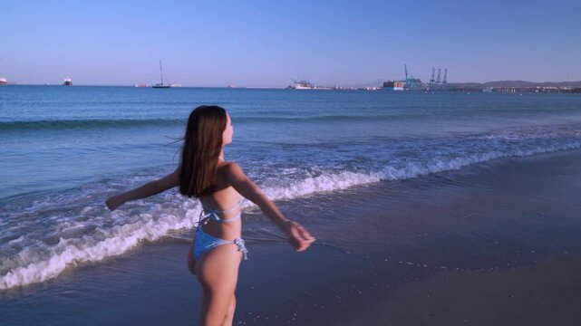 Chica joven dando vueltas con los brazos levantados muy feliz por su sensacional d&iacute;a de sol y playa en verano al atardecer.