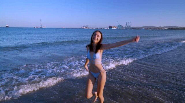 Chica joven muy contenta en la playa dando vueltas, saltos y jugando con el agua sonriendo, por su sensacional d&iacute;a de sol y mar en vacaciones.