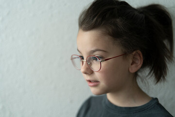 Fototapeta premium little sad girl in glasses standing near white wall. Upset child concept