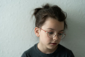 little sad girl in glasses standing near white wall. Upset child concept