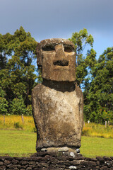 Fototapeta premium Moai de pie sobre base piedras, al fondo arboles verdes y pascto