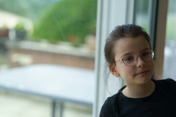 little cute girl with glasses standing near big window. Smart conscious child concept