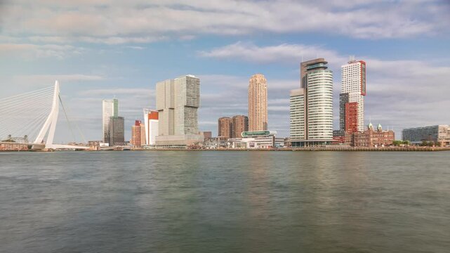 Panorama showing Rotterdam skyline timelapse from Nieuwe Maas River bank to Wilhelminapier and Kop van Zuid. Modern skyscrapers, ship terminal and Erasmus Bridge, waterfront with boats passing by