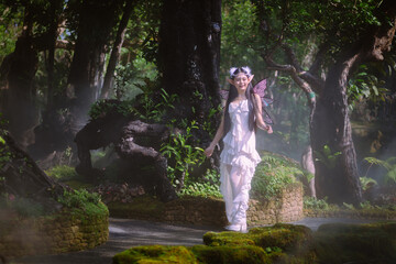 Portrait fantasy Angel Fairy Tale woman in forest natural trees. Elf girl fashion in pink dress with butterfly wings fairy tale story world. Walks in fresh green trees with magic radiance.