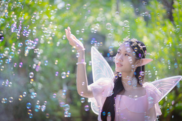 Portrait fantasy Angel Fairy Tale woman in forest natural trees. Elf girl fashion in pink dress with butterfly wings fairy tale story world. Walks in fresh green trees with magic radiance.
