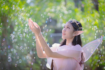 Portrait fantasy Angel Fairy Tale woman in forest natural trees. Elf girl fashion in pink dress with butterfly wings fairy tale story world. Walks in fresh green trees with magic radiance.