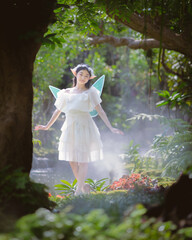 Portrait fantasy Angel Fairy Tale woman in forest natural trees. Elf girl fashion in pink dress with butterfly wings fairy tale story world. Walks in fresh green trees with magic radiance.