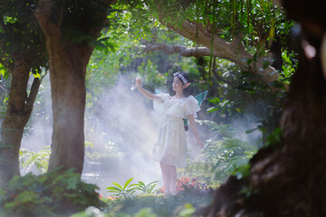 Portrait fantasy Angel Fairy Tale woman in forest natural trees. Elf girl fashion in pink dress with butterfly wings fairy tale story world. Walks in fresh green trees with magic radiance.
