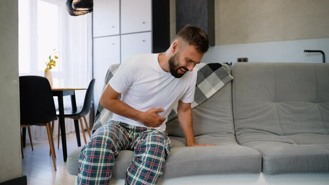 A Man with Stomach Pain Clutches Abdomen in Discomfort at Home