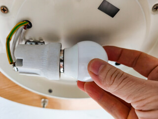 A hand changing the light bulb. Screwing an energy efficient LED light bulb into the socket....