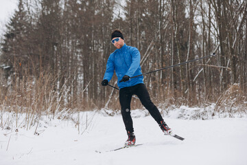 Male skier enjoying a downhill ride on a cross-country trail in the winter forest