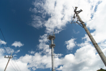 送電線と携帯電話のアンテナと防災無線のスピーカーの柱