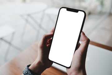 Close-up of hands holding a smartphone with a blank screen, ready for customization. The background features a casual workspace with soft natural light and a wooden desk.