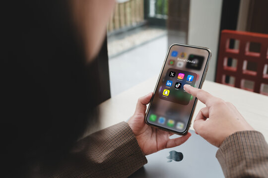 Bangkok, Thailand. December 10, 2024; A person scrolling through social media apps like Facebook, Instagram, TikTok, and LinkedIn on a smartphone in a casual workspace by the window.