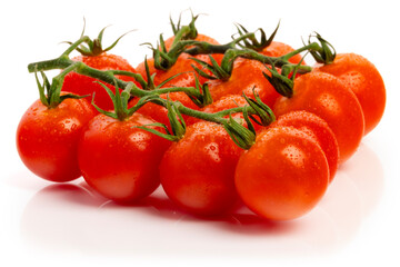A bunch of juicy, wet cherry tomatoes on the vine sitting on a reflective, white background.