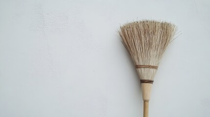 Broom leaning against a clean white wall showcasing its natural bristles and minimalist design for home cleaning and organization use