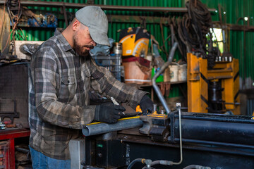 A metal worker carefully measures a pipe in a workshop, showcasing precision in craftsmanship