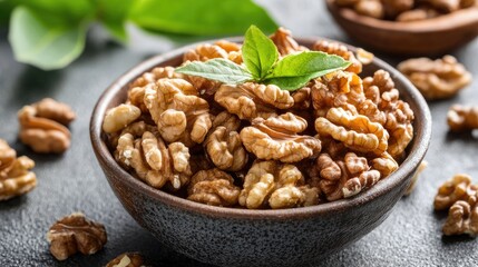 Obraz premium Healthy walnuts in bowl with fresh mint garnish on rustic stone background showcasing natural ingredients and nutritious snacks.