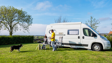 A man and his faithful dog stand next to an RV or camper van in a picturesque grassy field in Texel...