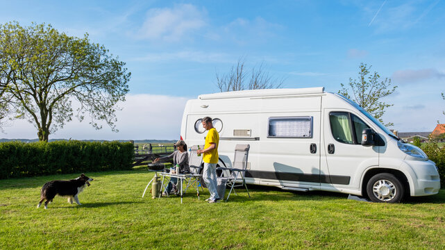 A man and his faithful dog stand next to an RV or camper van in a picturesque grassy field in Texel Netherlands, soaking in the serenity of their surroundings. a couple at a camping farm