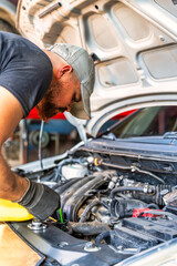 A car mechanic diligently working underneath the vehicles hood in a bustling auto repair shop