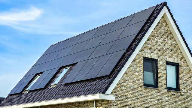 Newly built houses with black solar panels on the roof against a blue sunny sky Close up of new building with black solar panels. Zonnepanelen, Zonne energie, Translation: Solar panel, Sun Energy