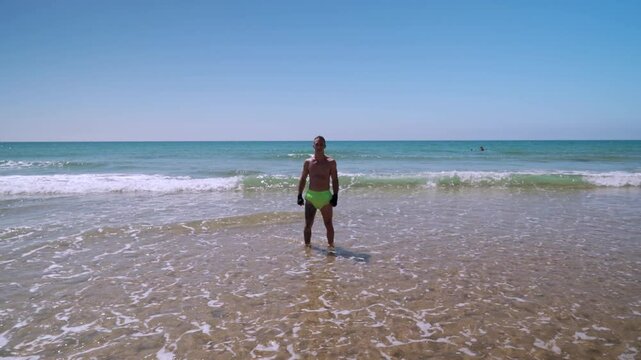 Hombre luchador en artes marciales con los ojos cerrados en la orilla de la playa con las olas del mar, abre los ojos y comienza a hacer ejercicios de lucha.