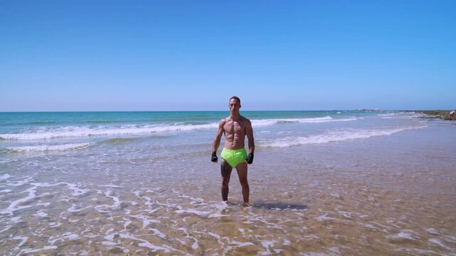 Hombre luchador en artes marciales con los ojos cerrados en la orilla de la playa con las olas del mar, abre los ojos y comienza a hacer ejercicios de lucha.