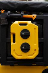 Vertical close up photo. Yellow plastic canister for liquid, gasoline, water with capacity of 2.6 gallons, 10 liters, an axe hang on trunk of an SUV. Concept of travel, adventure, trip. Off-road car