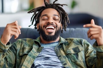 Happy man with dreadlocks smiling broadly while relaxing on a couch in a modern living room, showcasing joy and comfort in everyday life