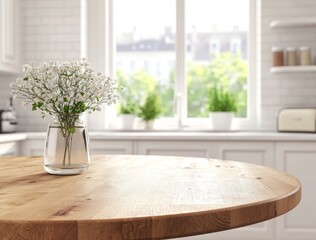 White flowers in glass vase on round wooden table in bright kitchen.