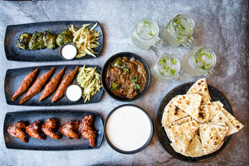 Chicken Hariyali Kebab, Chicken Seekh Kebab, Chicken Wings, Beef Korma, Garlic Nan, Rita, Salad and Mint Lime Mojito isolated on grey background top view of Indian and Bangladeshi food