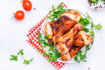 Baked chicken legs or drumsticks in spices with parsley on plate, white table background, top view