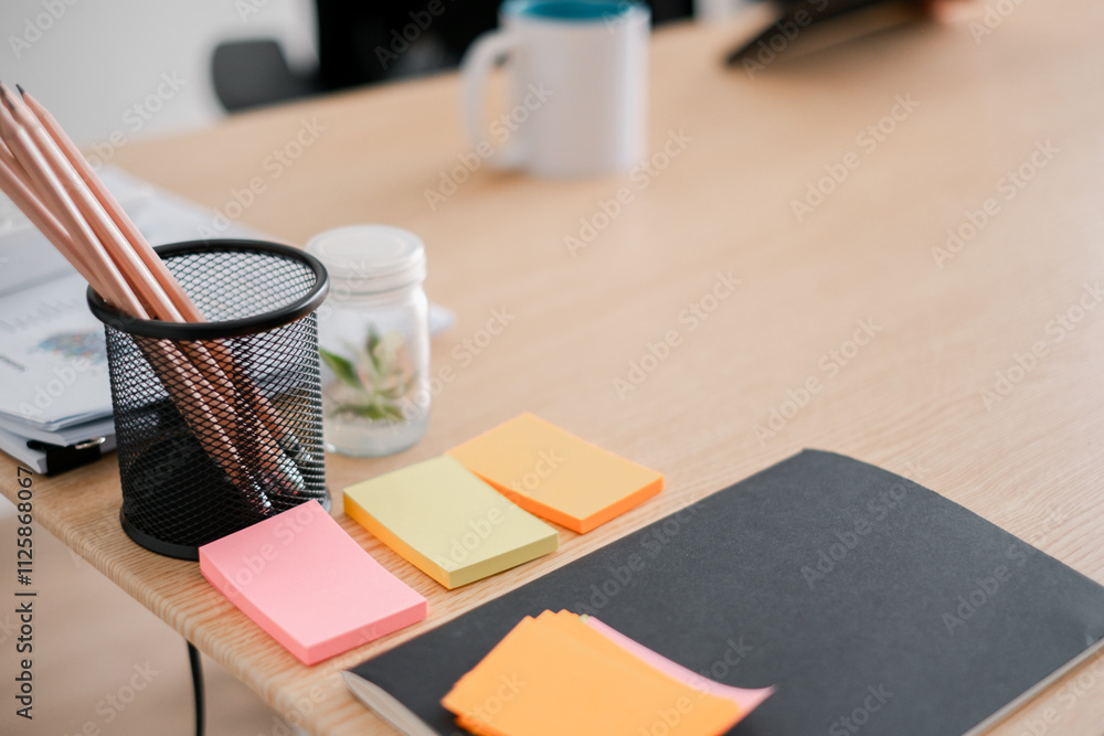 Poster a tidy office desk featuring colorful sticky notes, pencils in a holder, and a notebook, ideal for p