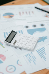 A white calculator placed on financial documents with graphs and charts, symbolizing business analysis and financial planning.