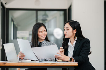 Two businesswomen discussing documents in a contemporary office setting, showcasing teamwork and collaboration.