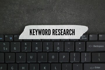 laptop keyboard and sticker with the word keyword research. process of finding and analyzing search...