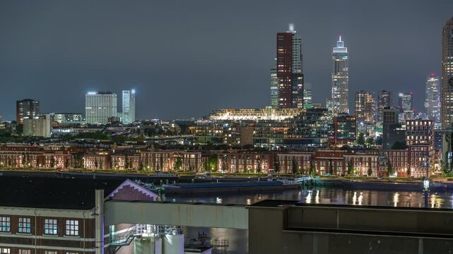 Panoramic aerial timelapse of Katendrecht peninsula and Maashaven harbour at night in Rotterdam, The Netherlands. City skyline, illuminated modern skyscrapers and former factory with waterfront houses