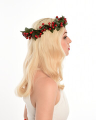 Naklejka premium close up portrait of beautiful blonde female model wearing holly and ivy Christmas fantasy wreath crown headdress. isolated silhouette, looking away in side profile on white studio background.