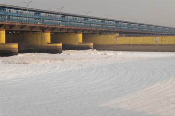 polluted river with industrial and domestic effluents toxic foam and road bridge at morning